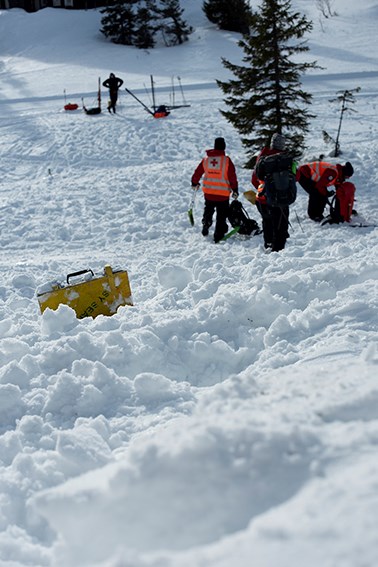 En gul koffert ligger i snøen, i bakken bak står en gruppe mennesker med Røde Kors-uniform.