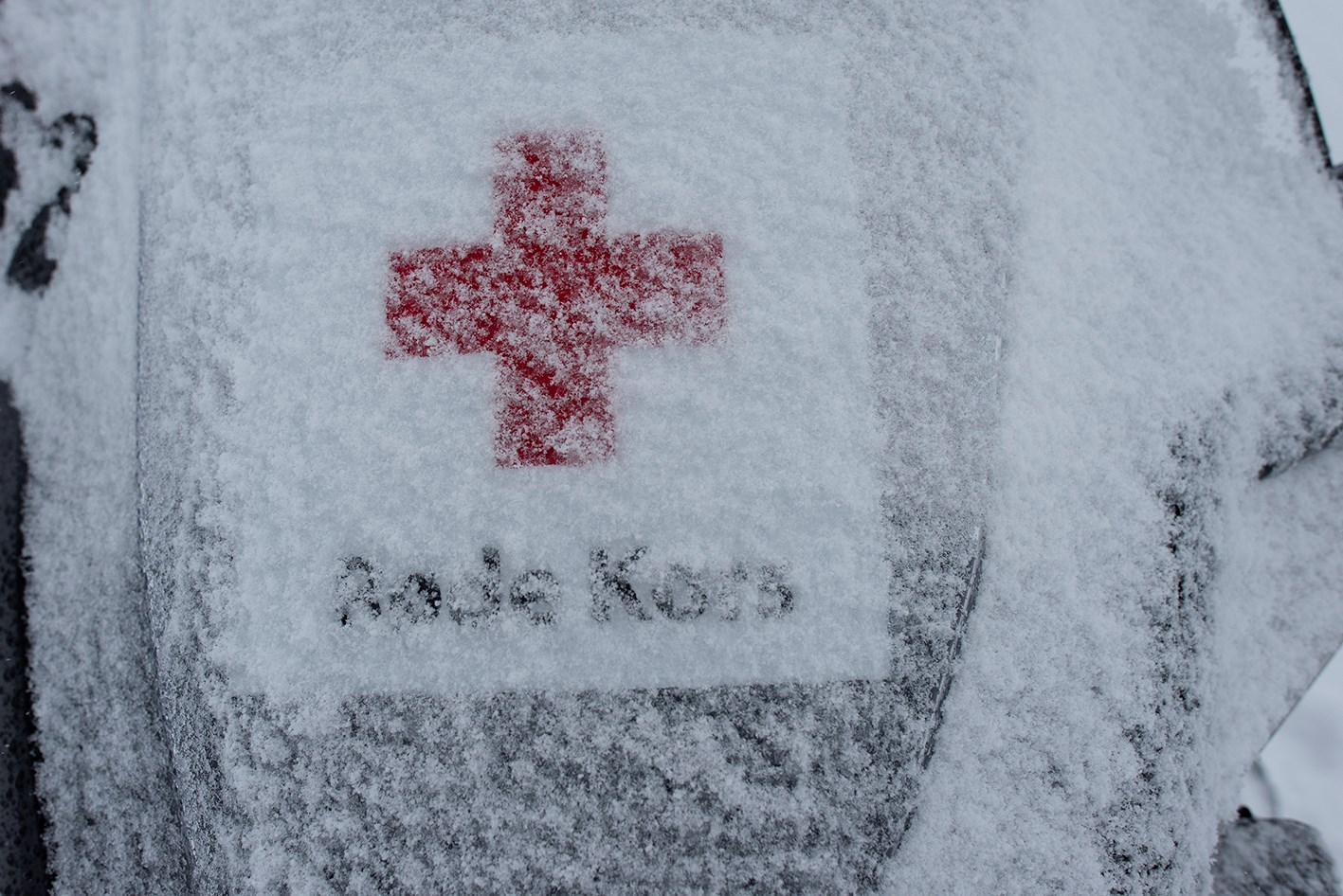 Røde Kors-logo på vinduet til en snøscooter. logoen er nesten helt dekket til av snø.