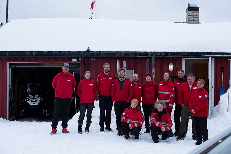 En gjeng hjelpekorpsene står utenfor en hytte i snøen. alle smiler