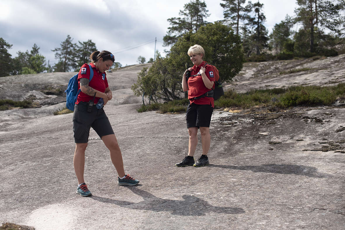 To damer i Røde Kors-uniform står i en fjellskrent. De har sekker på ryggen.