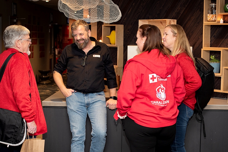 En mann står og prater med tre frivillige rundt seg. De smiler og ler.