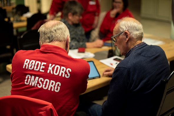 To menn sitter med ryggen til og jobber med en pad