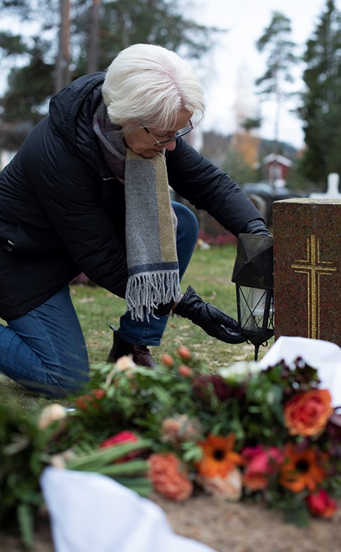 En dame kneler ved en grav. Det er tidlig vinter og det ligger noen få blomster på grava.