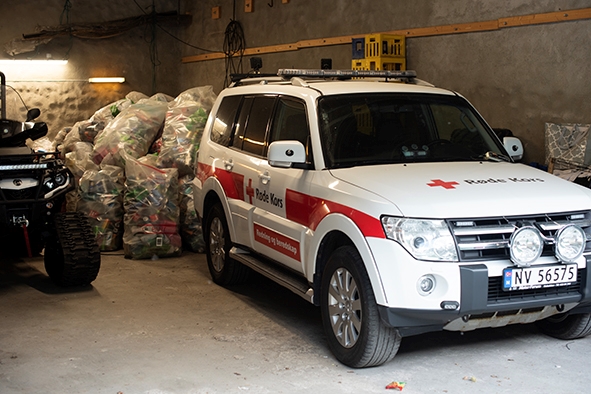 En Røde Kors-bil og en arv står i en garsajse. Bak bilen står det poser med pant.