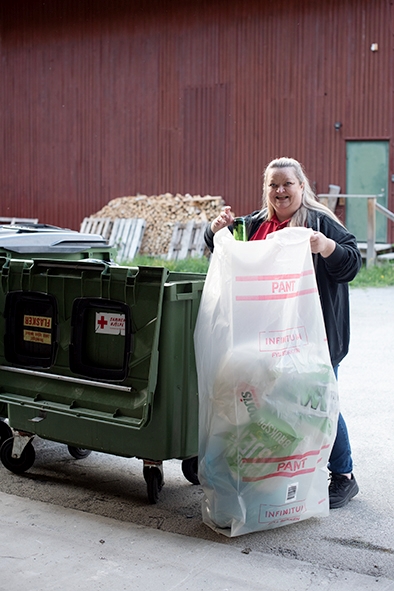 dame står med en søppelsekk foran en pantekontainer.
