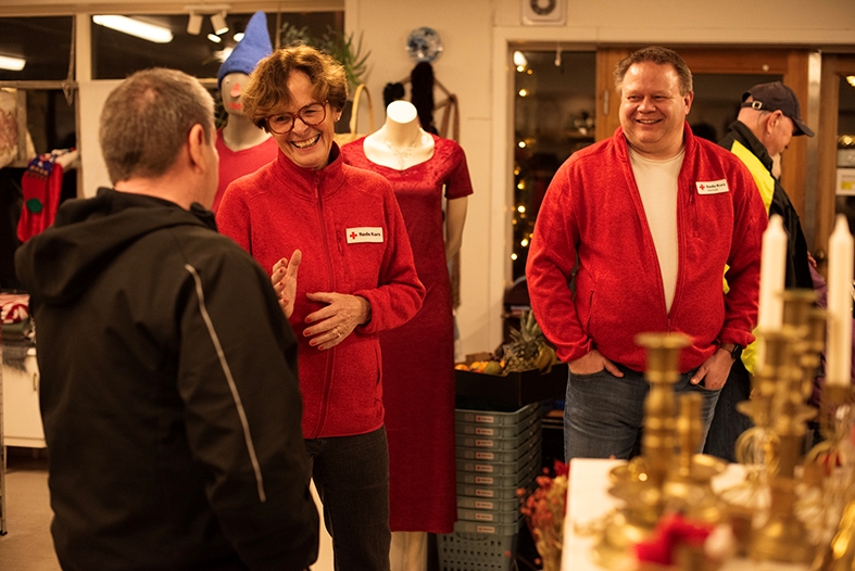 Tre personer snakker sammen og ler i et butikklokale. To med Røde Kors-klær står med ansiktet mot kamera, den tredje har sivile klær og står med rygget til.