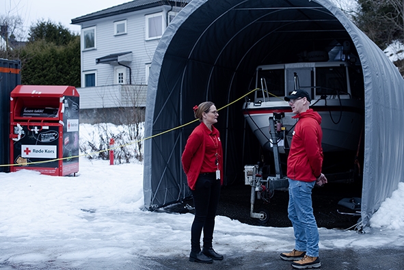 To personer i Røde kors-klær står utenfor et telt med en båt. Det er vinter. 