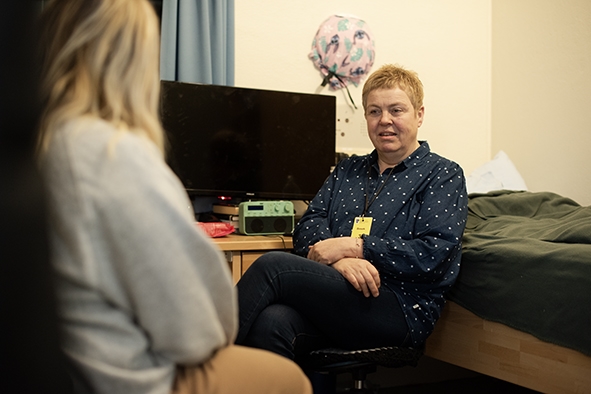 En dame sitter på et lite rom i samtale med en annen dame som har rygget til og er anonym