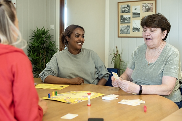 Tre damer spiller brettspill ved et bord.