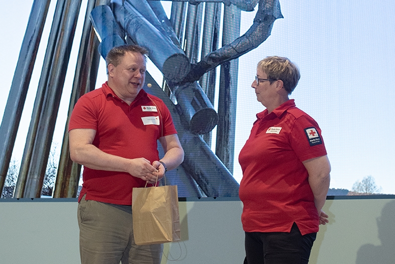 En mann og en dame står og prater foran et bilde av tømmerfløtestatuen i Skien.