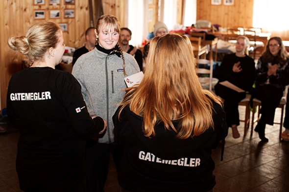 Bilde av en jente som smiler, en dame med gatemeiglingsgenser står med ryggen mot kamera.. Jenta får tildelt diplom