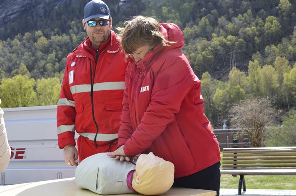 En dame trener på lungekompressjoner. En mann i Røde Kors-uniform står ved siden av og veileder.