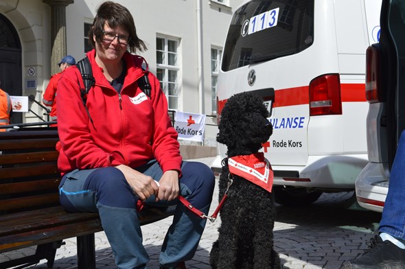 En dame i Røde Kors-klær sitter sammen med hunden sin som er besøksvenn foran en beredskapsbil fra Røde Kors.