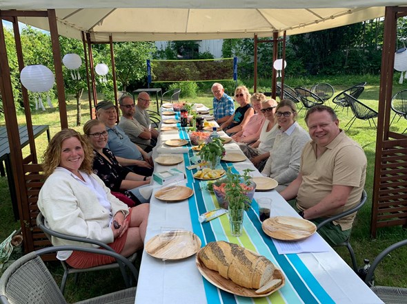 10 mennesker sitter rundt et festdekket bord i en hage. 