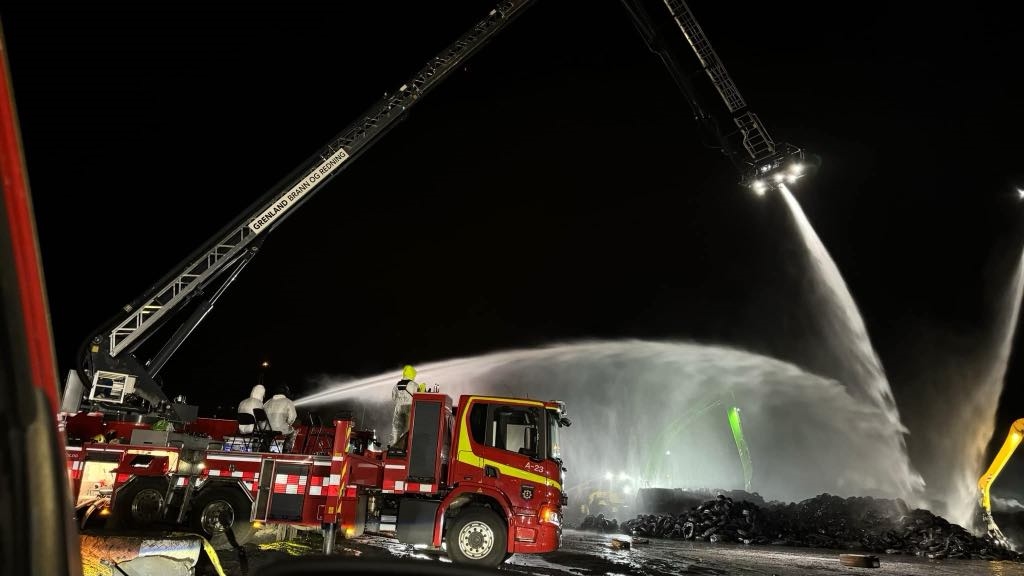 En brannbil står og spruter vann på gummidekk. Det er natt.
