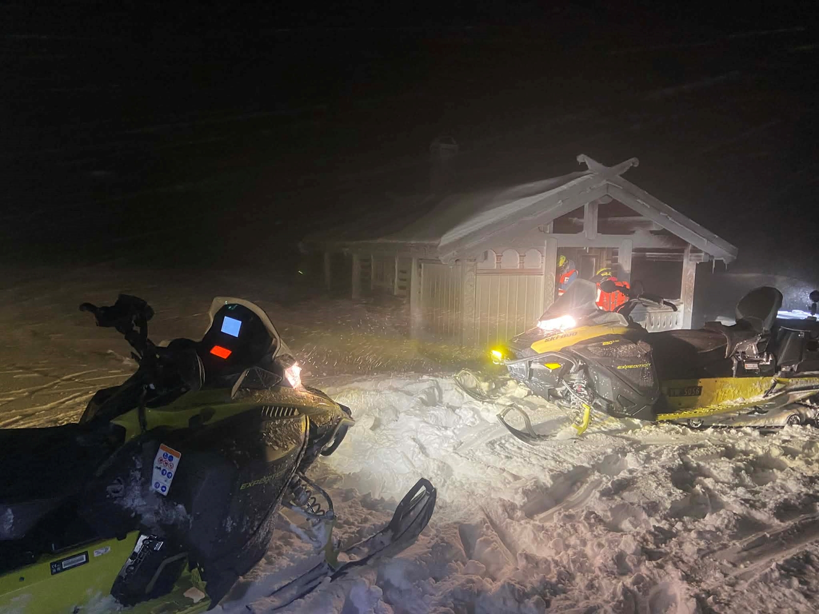 En hytte i vinterstorm. To scootere står utenfor. Det er natt.