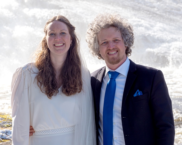 Et brudepar står foran en foss i brudestasen.