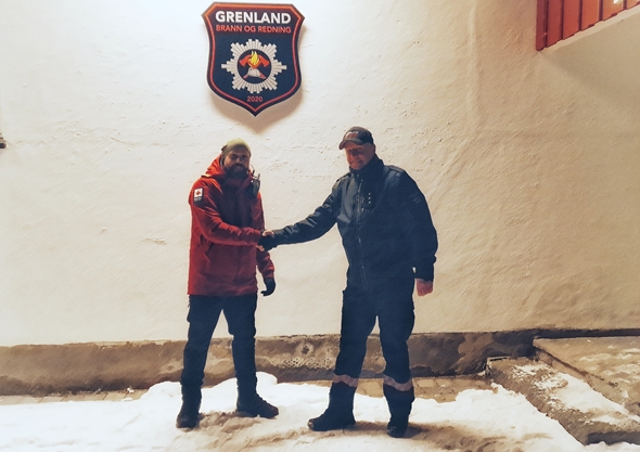 To menn står utenfor et hus i mørket og tar hverandre i hendene.