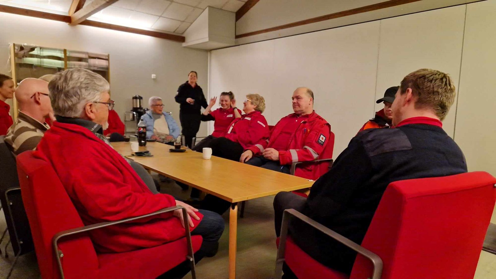 Røde Kors-kledde mennesker sitter rundt et bord og prater