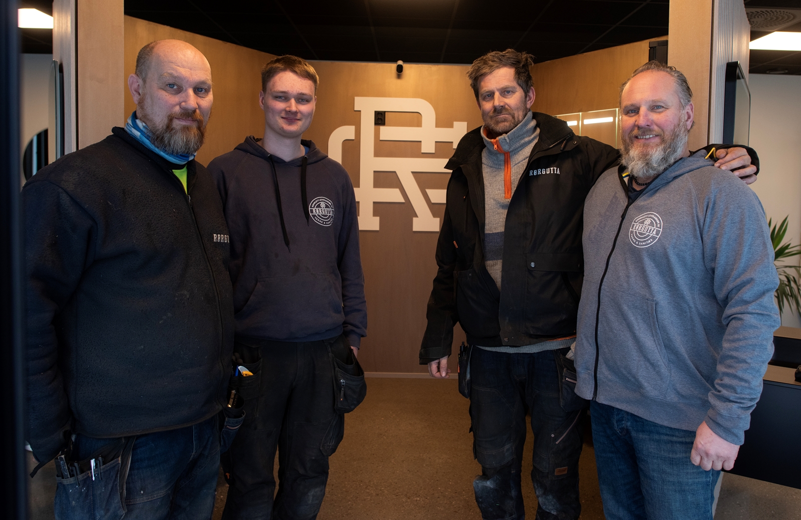 Gruppebilde av fire menn som står foran en baderomsutstilling