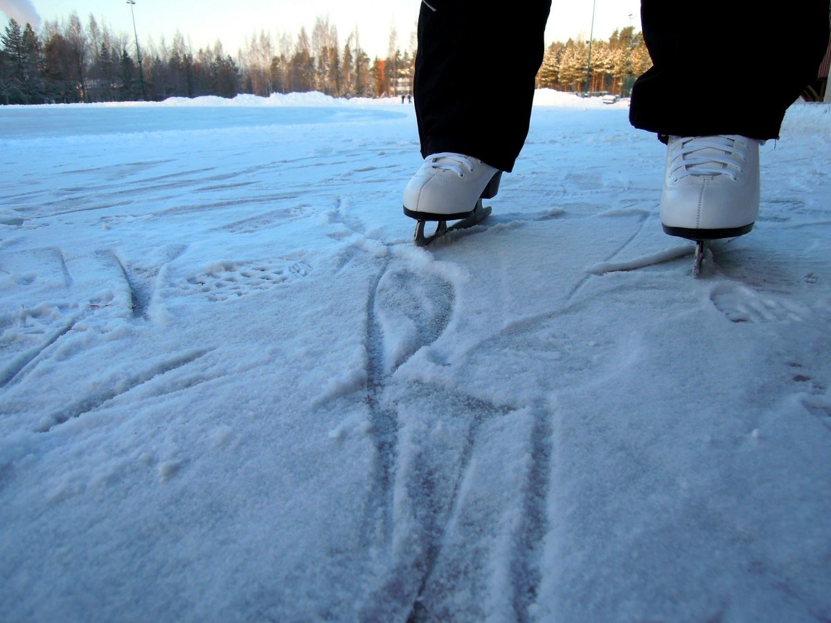Noen står på skøyter på snødekt vann. En ser bare beina. Bildet er tatt i froskeperspektiv.
