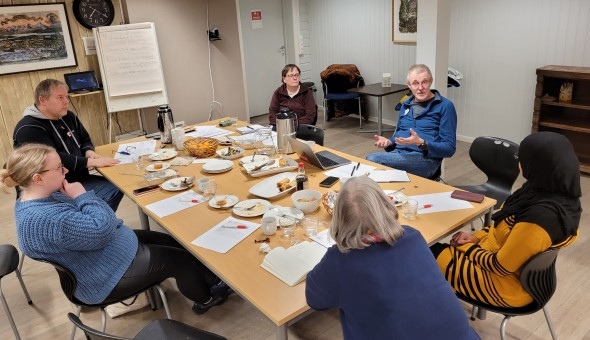 En gruppe mennesker sitter rundt et bord og diskuterer.