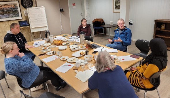 En gruppe mennesker sitter rundt et bord og diskuterer.