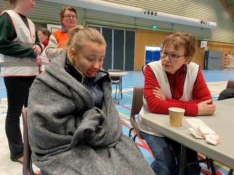 Bildet viser en person som får et pledd rundt seg og omsorg fra en kvinne som er frivillig i Røde Kors.