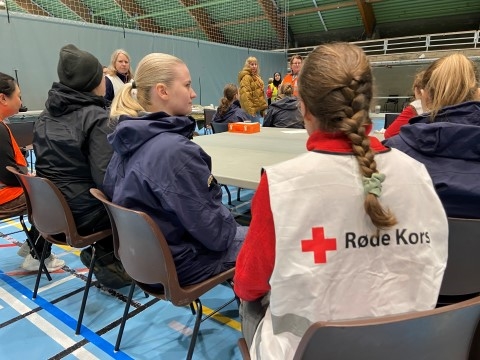 Bildet viser en frivillig i Røde Kors-vest som sitter i en gruppe med mennesker og som deltar i en beredskapsøvelse.
