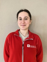 Lidiia ser mot kamera og smiler. Hun har på seg en rød genser med Røde Kors-logo.