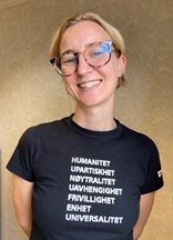 Sunniva ser mot kamera og smiler. Hun har på seg en svart t-skjorte med Røde Kors-logo.