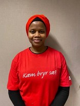 Bata Diallo ser mot kameraet og smiler. Hun har på seg en rød tskjorte med påskriften "Kæm bryr sæ?". 