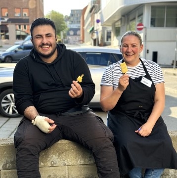 En mannlig deltaker og en kvinnelig frivillig sitter på en benk og spiser is. De smiler bredt til kamera.