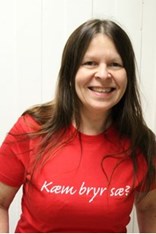 Karen Nilsen ser mot kameraet og smiler, i en rød tskjorte med påskriften "Kæm bryr sæ?". Foto.
