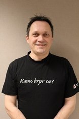 Kjell Roger Andersen ser mot kameraet og smiler, i en svart tskjorte med påskriften "Kæm bryr sæ?". Foto.