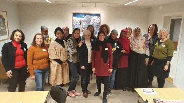 Bildet viser 16 kvinner fra ulike kulturer. Noen har hodeplagg på, andre ikke. De står sammen og smiler til kamera.