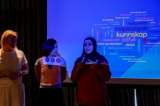 Bildet viser tre kvinner som står på en scene foran en stor forsamling.