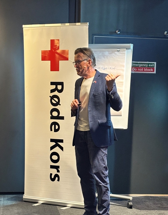 Bildet viser en mann stå på en scene foran en forsamling.