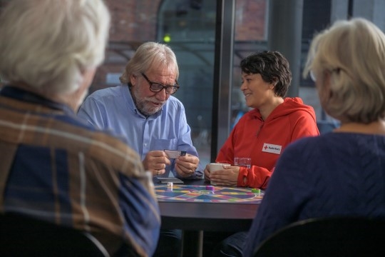 Bildet viser tre eldre mennesker som spiller spill med en frivillig fra Røde Kors.