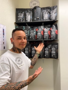 Deltaker i Nettverk etter soning står foran hylle med kaffeposer og smiler til kamera.