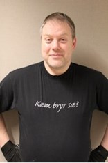 Odd-Bjørn Sørnes ser mot kameraet og smiler, i en svart tskjorte med påskriften "Kæm bryr sæ?". Foto.