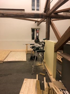 Bildet viser et lokale som er under ombygging. Det står en sag på gulvet og masse treplanker ligger på gulvet.