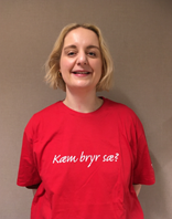 Pernille ser mot kamera og smiler. Hun har på en rød t-skjorte. På t-skjorta står skriften "Kæm bryr sæ?".