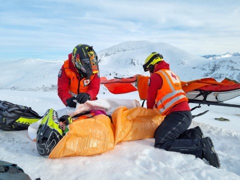 Bildet viser to personer kledt i Røde Kors-bekledning. De er på fjellet. De har skuterhjelmer på og øver på redning i fjellet.