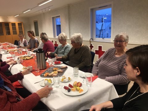Bildet viser flere eldre kvinner sitte rundt et bord. De drikker kaffe og spiser kake. De samtaler sammen og smiler.