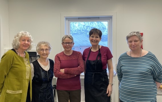 Bildet viser fem kvinner som smiler til kamera. Noen har forklær på.