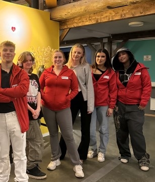 Bildet viser flere ungdommer stående på rekke med røde klær på. De smiler til kamera.