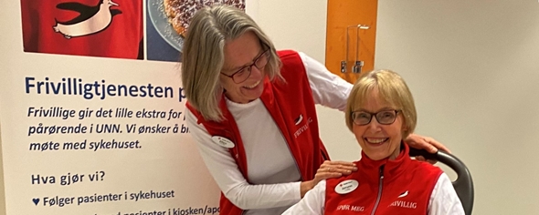 To frivillige kledt i røde vester smiler.