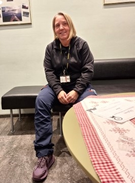 Bildet viser en kvinnelig fengselsbetjent som sitter på en sofa og smiler til kamera.