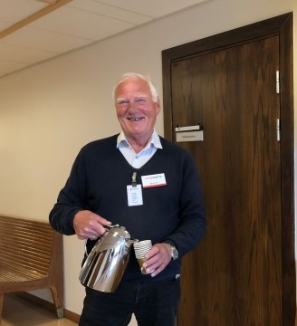 Bildet viser en mann som serverer kaffe. Han smiler.